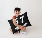 Smiling child hugging black 6-7 pillow with white number 67 design, funny teen gift idea